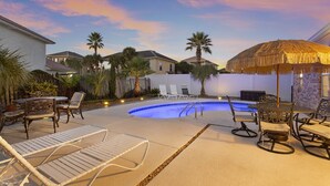 A backyard with a swimming pool, lounge chairs, a table, and a thatched umbrella. - Palm Breeze - Heated Private Pool, Deeded Beach Access, Free Beach Service! (Miramar Beach)