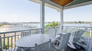 Une terrasse extérieure couverte, dotée d’une table et de chaises, qui offre une vue sur une marina et le bord de l’eau.