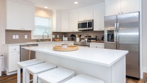 A modern kitchen with white cabinetry, stainless steel appliances, and a central island with seating. - Newly renovated home across from the beach! (Carolina Beach)