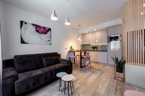 Un salon moderne avec un canapé foncé, une petite table et un coin cuisine équipé d’un micro-ondes et de placards.