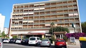 Een hotel met meerdere verdiepingen, balkons, een parkeerplaats en een winkelpand.