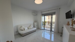 Een moderne woonkamer met een bank, een flatscreen televisie en een schuifpui naar een buitenruimte.