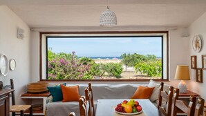 A dining area with a large window, wooden furniture, and a fruit plate on the table. - Villa Bay Pine - direct access to Pittulongu beach, wi-fi (Olbia)