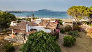 A coastal villa with a tiled roof, stone walls, and a garden with various plants and flowers. - Villa Bay Pine - direct access to Pittulongu beach, wi-fi (Olbia)