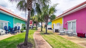 A courtyard with a paved walkway, outdoor seating, and palm trees.