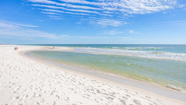 A wide sandy beach with clear blue waters and a few people walking.