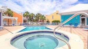 A swimming pool with a hot tub, surrounded by lounge chairs and a white fence.