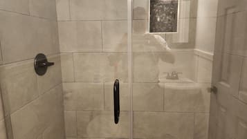 Eine bodenebene Dusche mit beigen Fliesen, einer Glastür und einem kleinen Spiegel über dem Waschbecken.