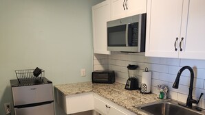 A compact kitchen with white cabinets, a stainless steel sink, a microwave, a toaster, and a refrigerator. - Harrison Hotel Unit E
Pet Friendly
Ground Level (Murrells Inlet)