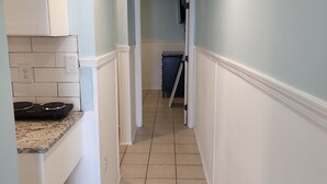 A narrow hallway with a kitchen area on the left, featuring a stove and cabinets. The walls are painted light blue, and the floor is tiled. - Harrison Hotel Unit E
Pet Friendly
Ground Level (Murrells Inlet)