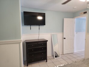 A room with a black dresser, a television mounted on the wall, and a door leading to another room.