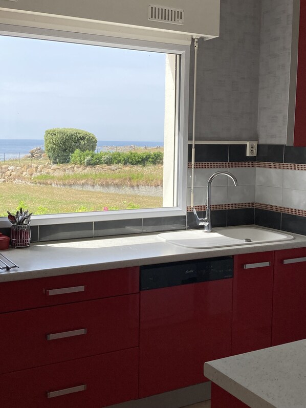 A modern kitchen with a large window overlooking a coastal landscape.