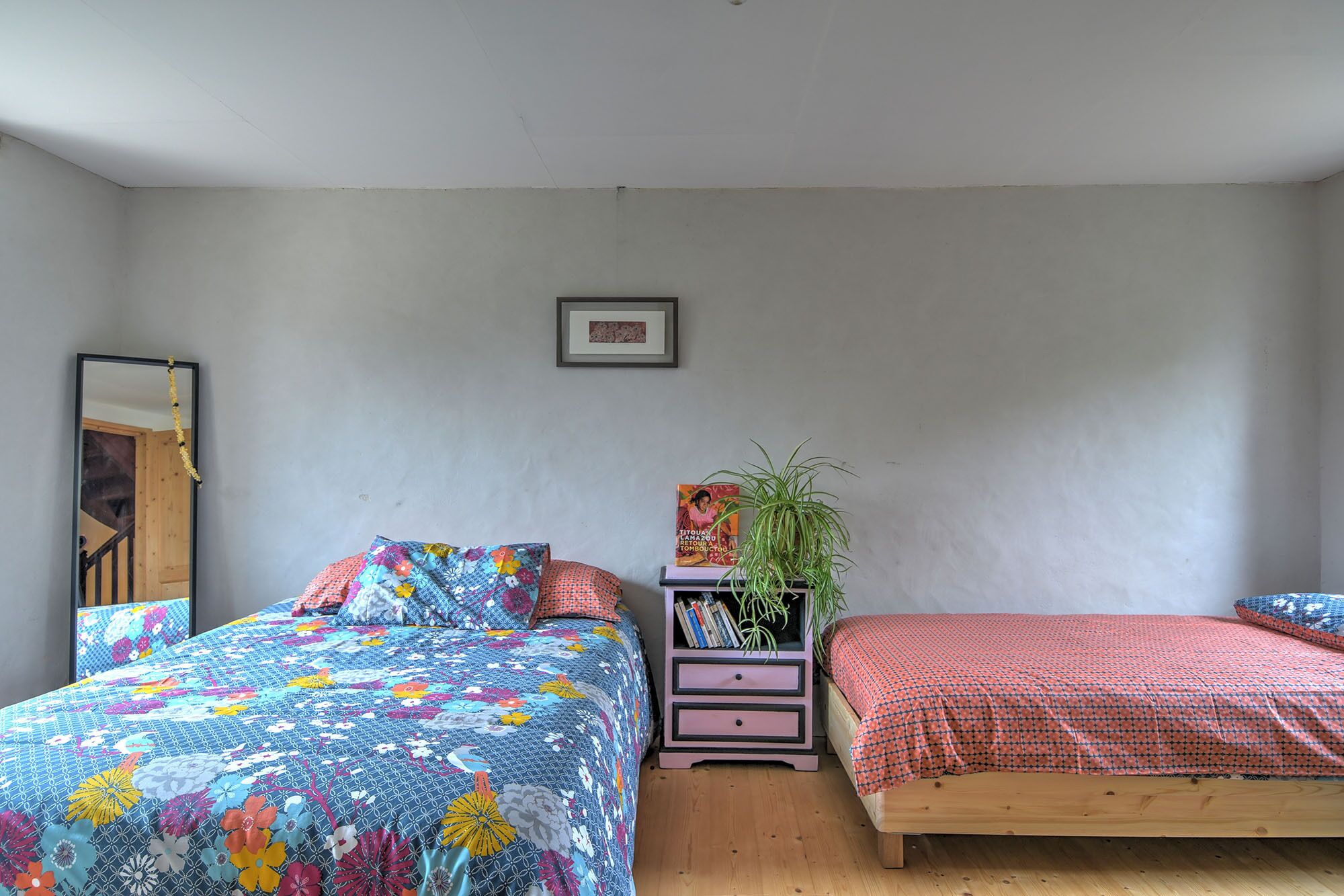 Een slaapkamer met twee bedden, een kaptafel, een spiegel en een ingelijste foto aan de muur.