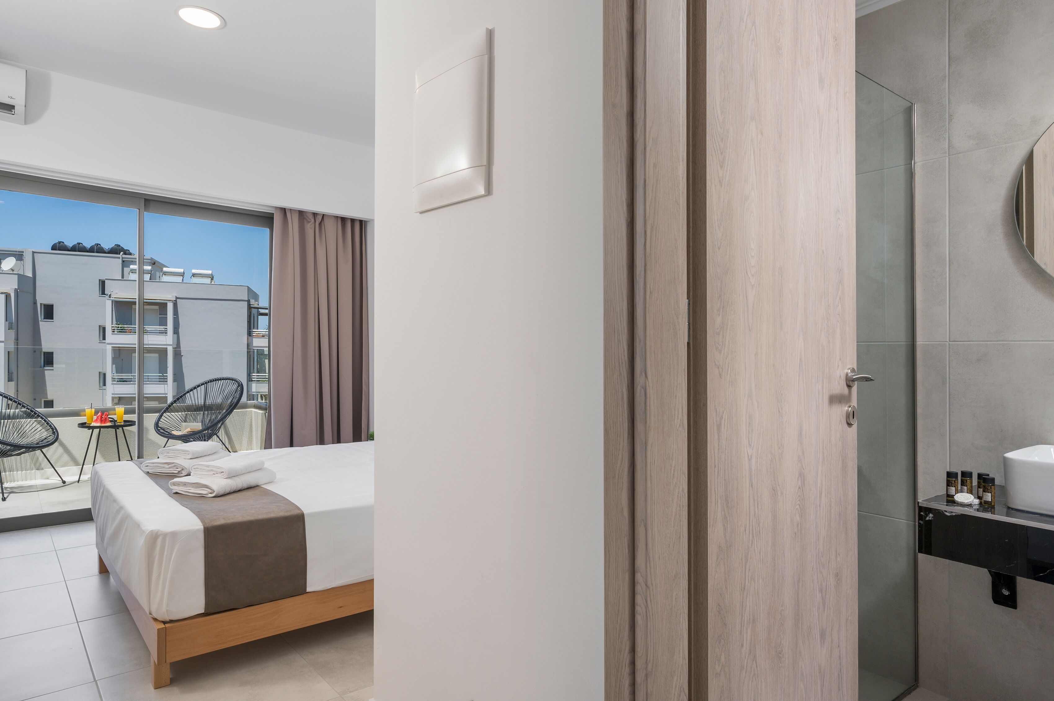 Een moderne hotelkamer met een bed, een klein tafeltje met stoel en uitzicht op gebouwen.