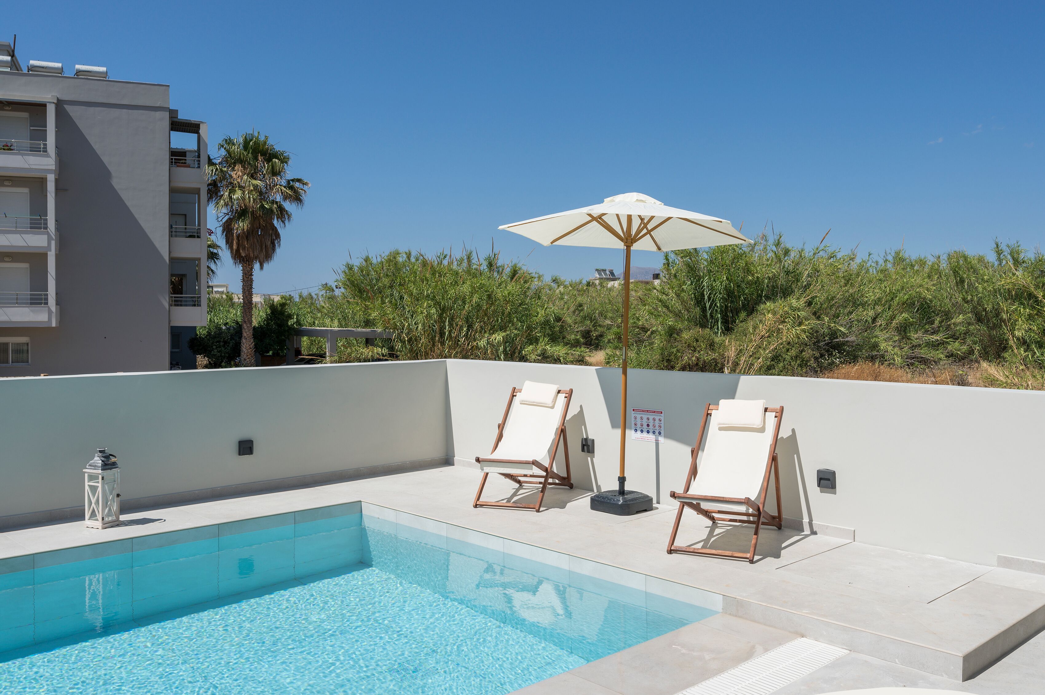 Un espace piscine sur le toit, avec deux chaises longues et un grand parasol, entouré de verdure et avec un bâtiment en arrière-plan.