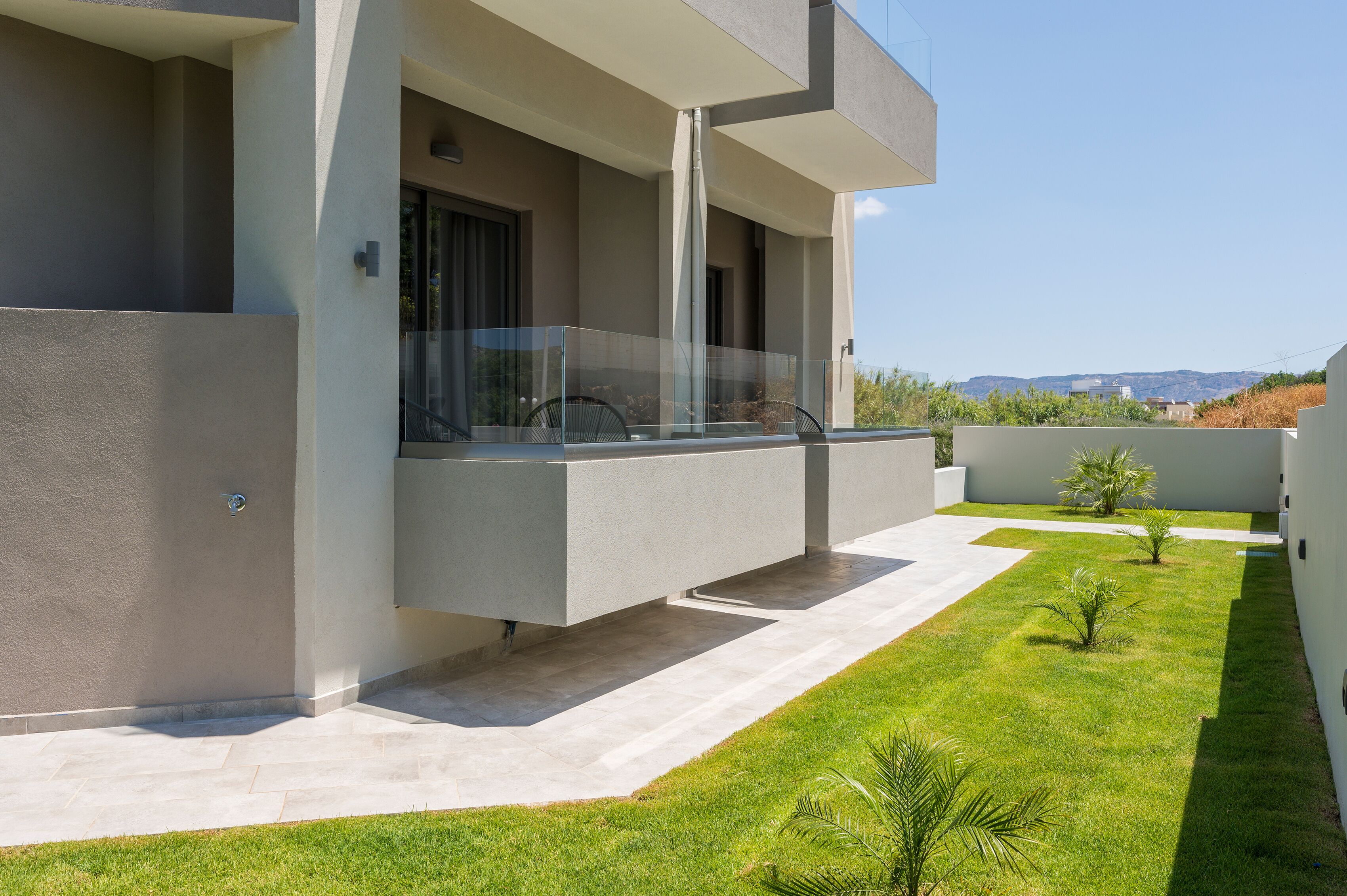 A modern building with a flat roof, a balcony with glass railings, and a well-maintained lawn.
