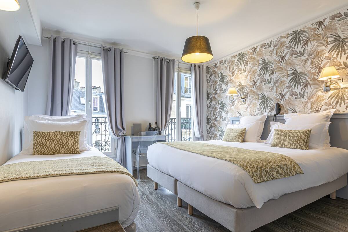 A hotel room with two beds, a desk, a TV, and a balcony with curtains.