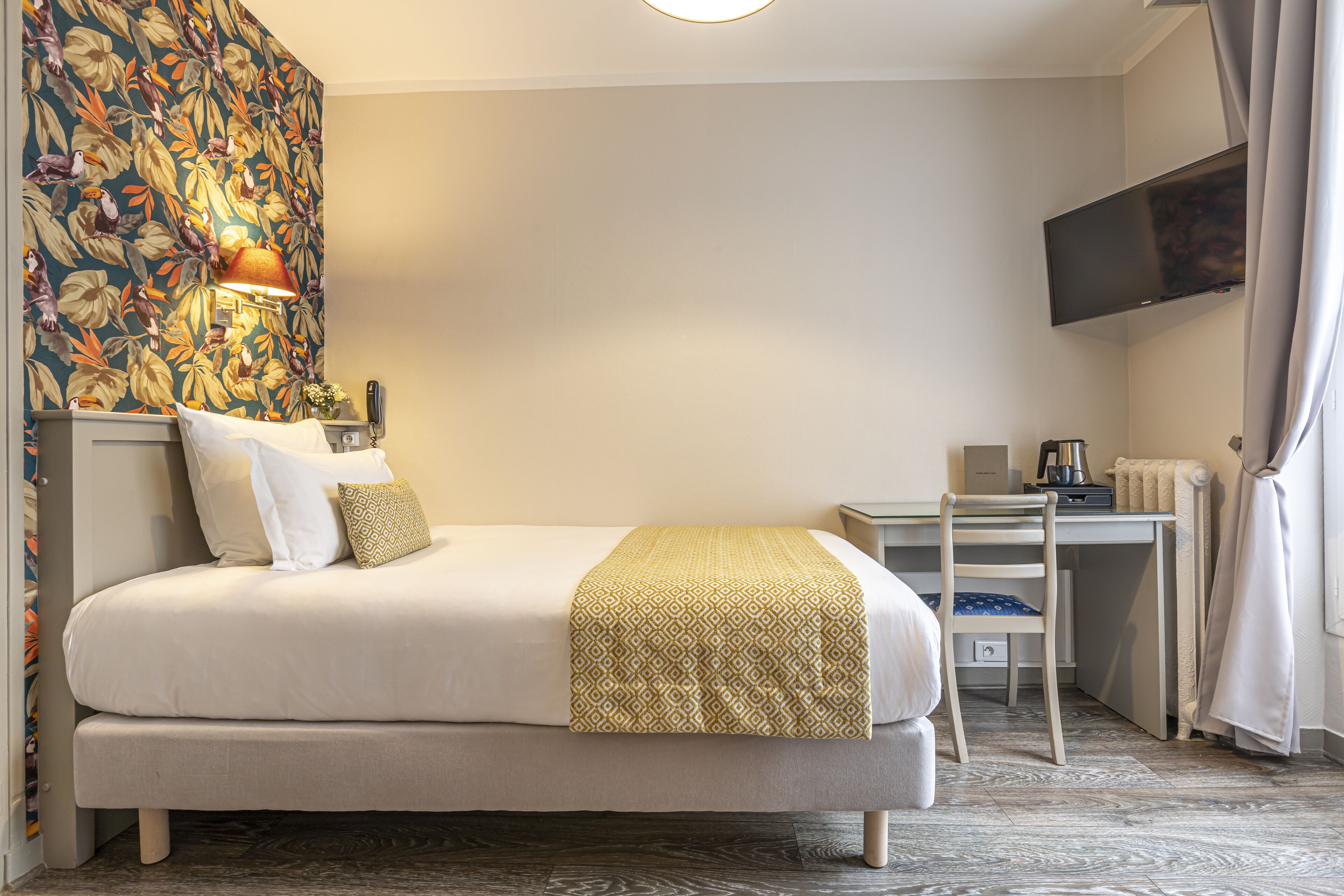 A hotel room with a bed, a desk, a chair, a TV, and a patterned wall.