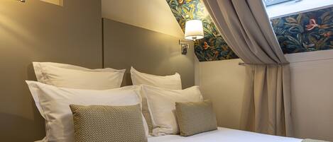 A neatly made bed with white and patterned pillows, a wall-mounted lamp, and a floral-patterned wall.