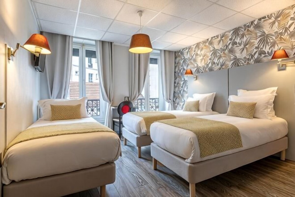 A hotel room with two beds, a desk, and a view of the city.