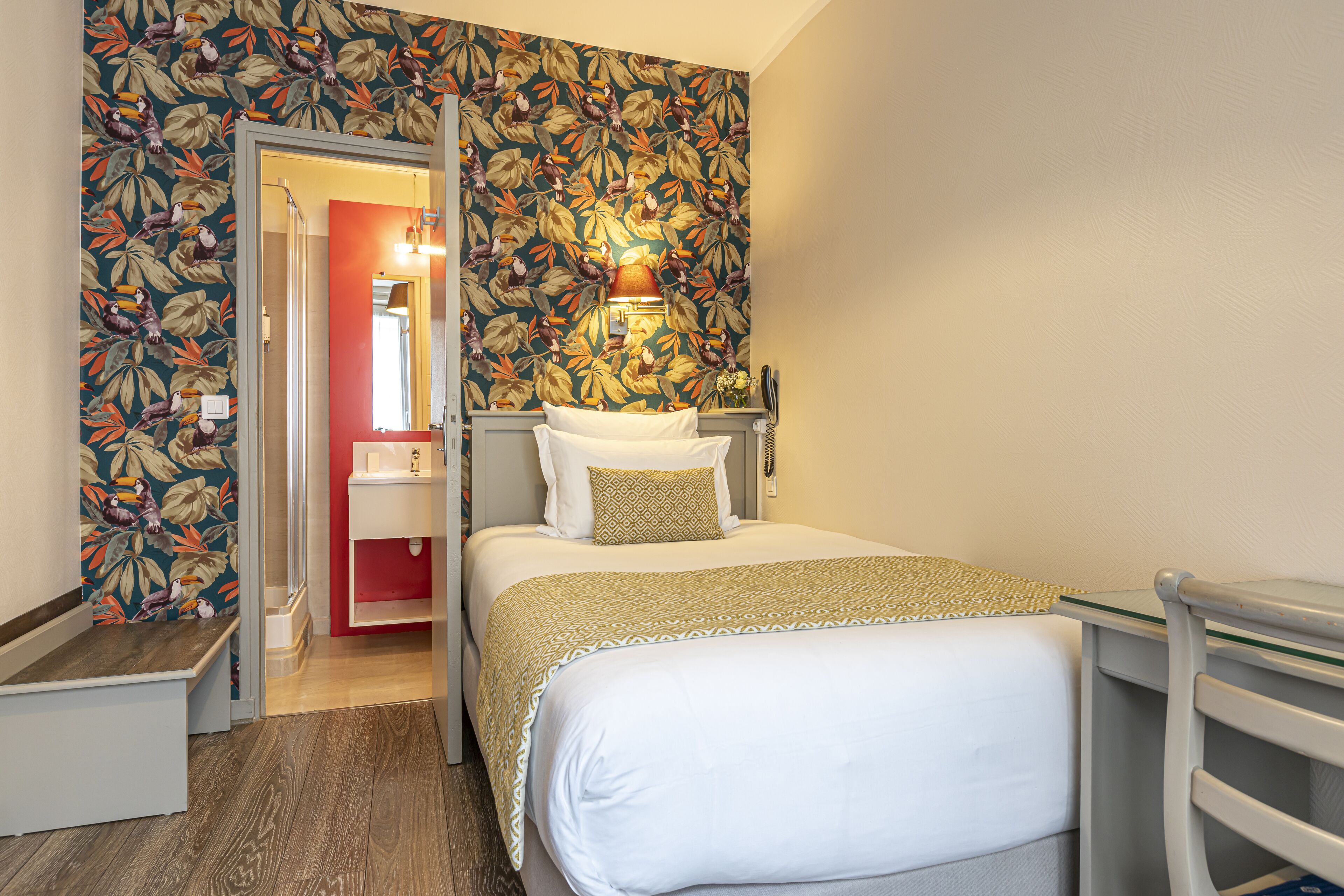 A hotel room with a bed, bedside table, and a mirror.
