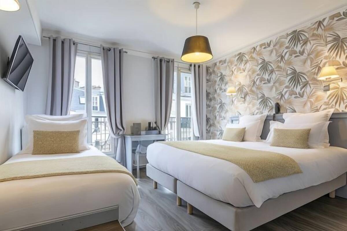 A hotel room with a large bed, a smaller bed, a desk, and a TV mounted on the wall.