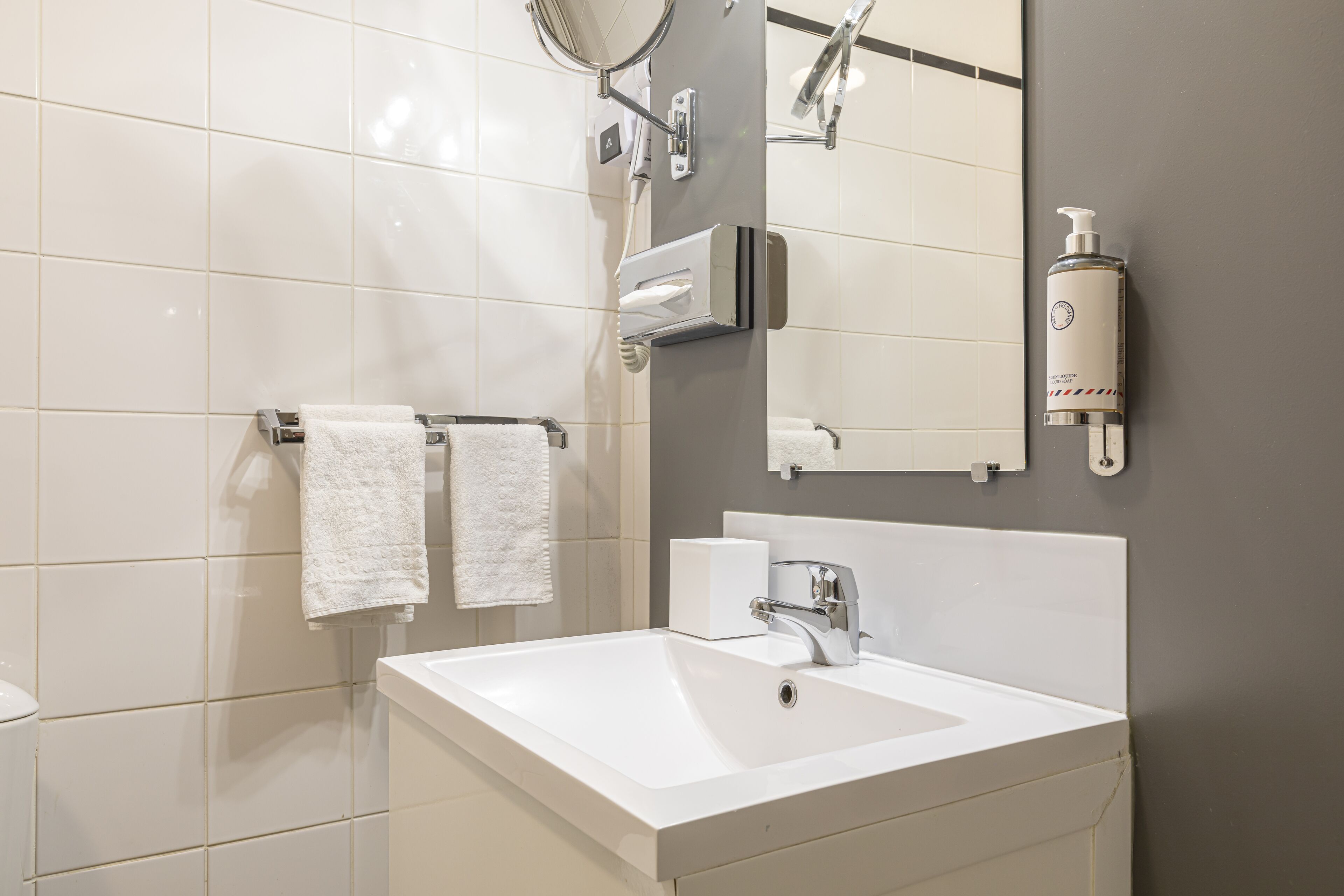 A modern bathroom with a white sink, a mirror, and two white towels hanging on a rack.