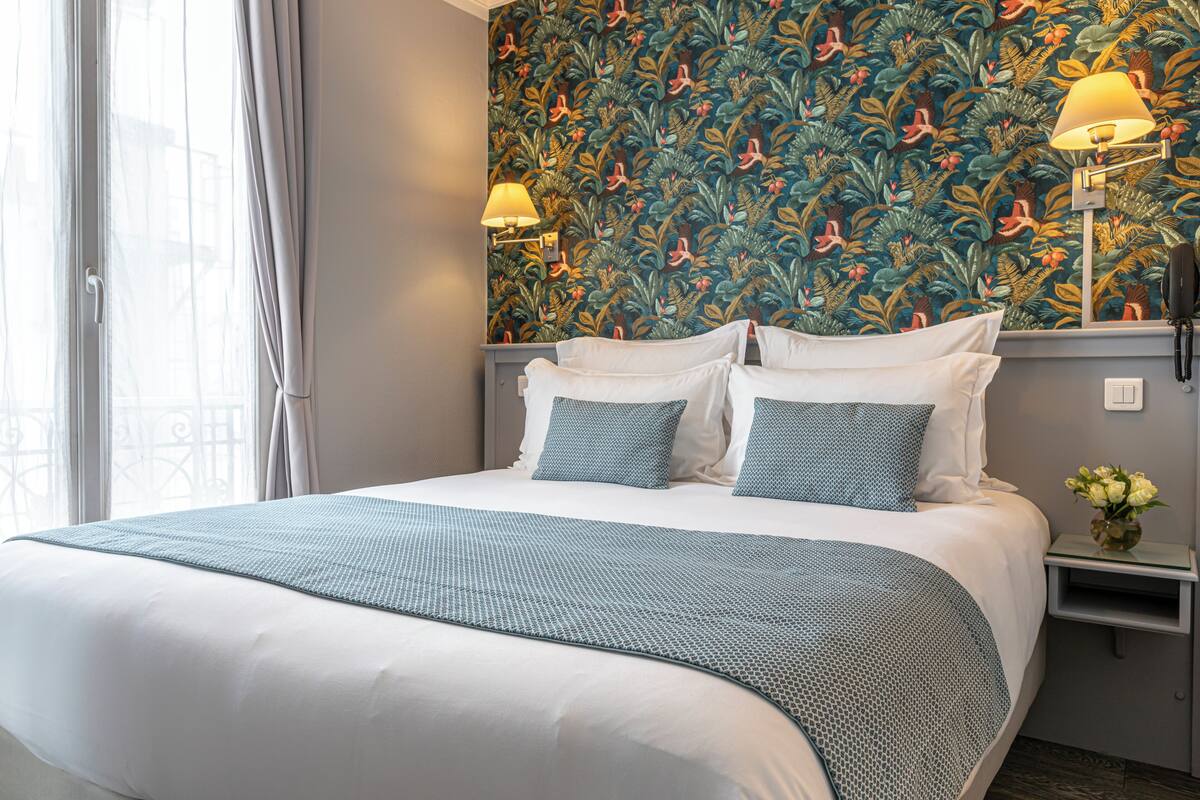 A hotel room with a large bed, two bedside lamps, a nightstand, and a floral wallpaper.