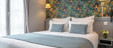 A hotel room with a large bed, two bedside lamps, a nightstand, and a floral wallpaper.