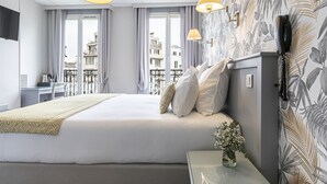 Une chambre d’hôtel avec un grand lit, un bureau et une vue sur les immeubles par les fenêtres.