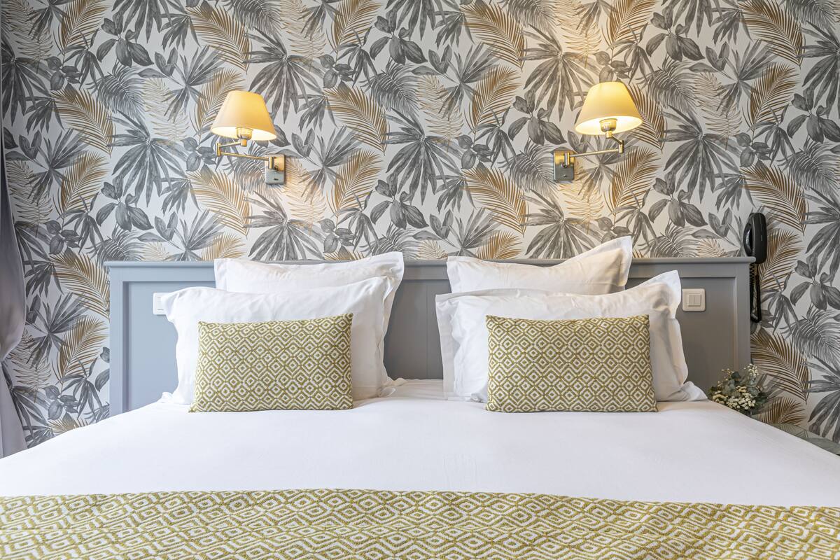 A hotel room with a bed, two wall-mounted lamps, and a patterned wallpaper.