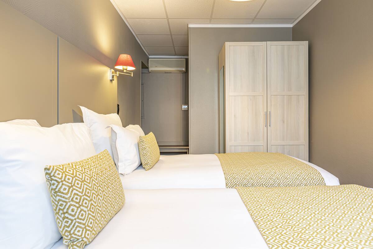 A hotel room with a bed, a wardrobe, and a wall-mounted lamp.