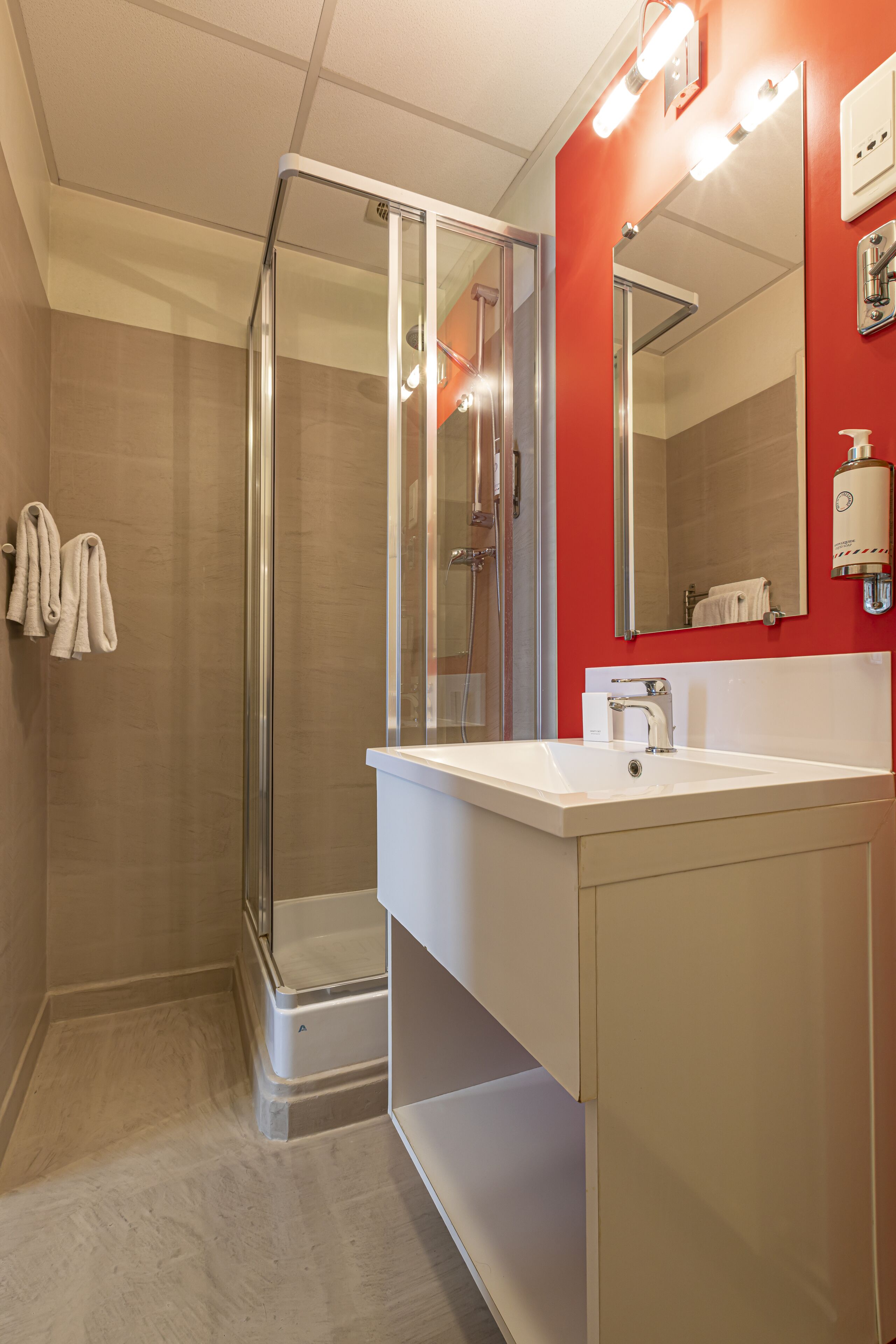 A modern bathroom with a glass-enclosed shower, a white sink, and a red accent wall.