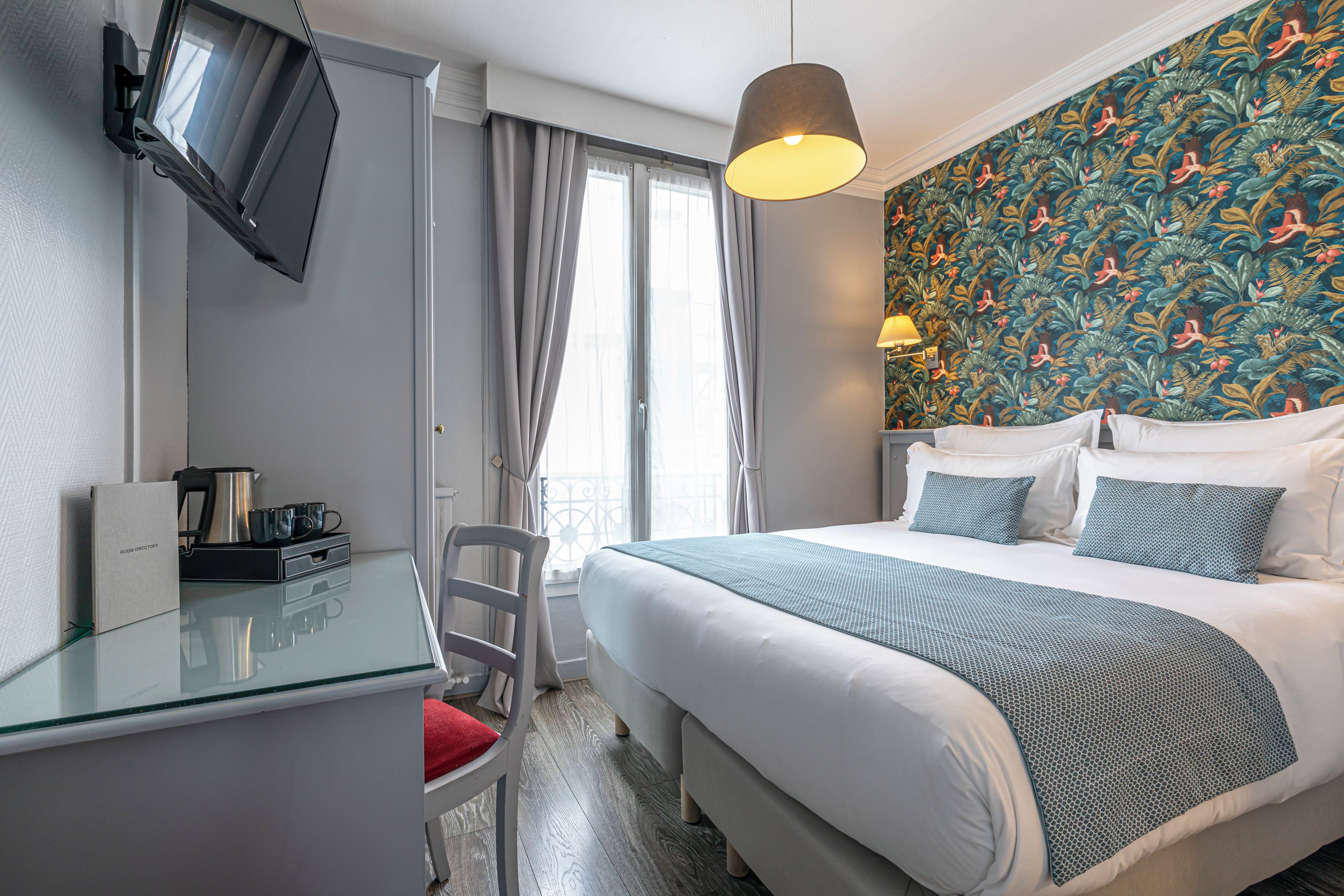 A hotel room with a bed, a desk, a chair, a TV, and a window with curtains.