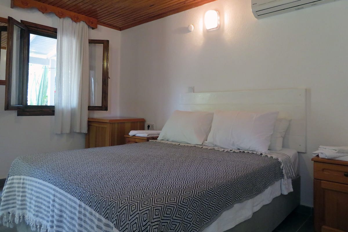 Un dormitorio con techo de madera, una cama con ropa de cama estampada, una mesita de noche, un espejo y un equipo de aire acondicionado.