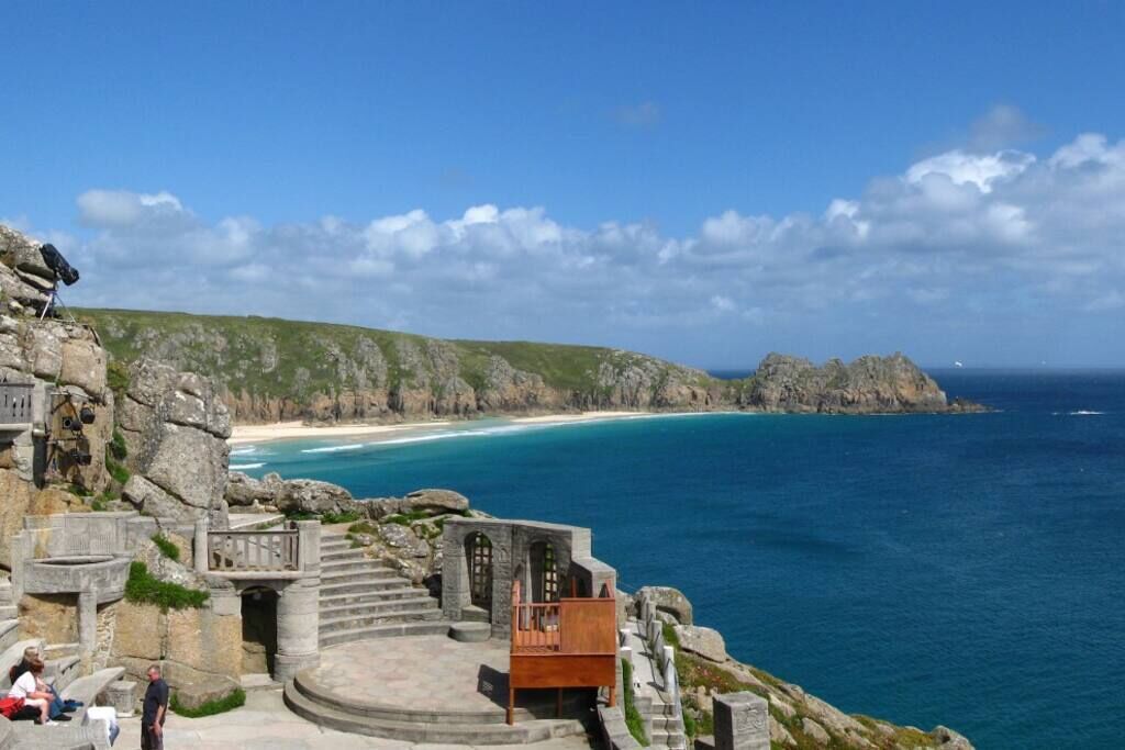 Una construcción costera de piedra con escaleras que llevan a un banco de madera, con vista a una playa y al océano.