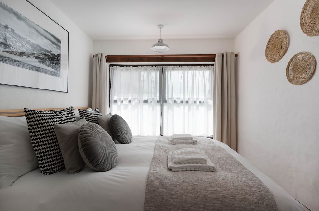 A bedroom with a bed, pillows, a blanket, and a window with curtains.