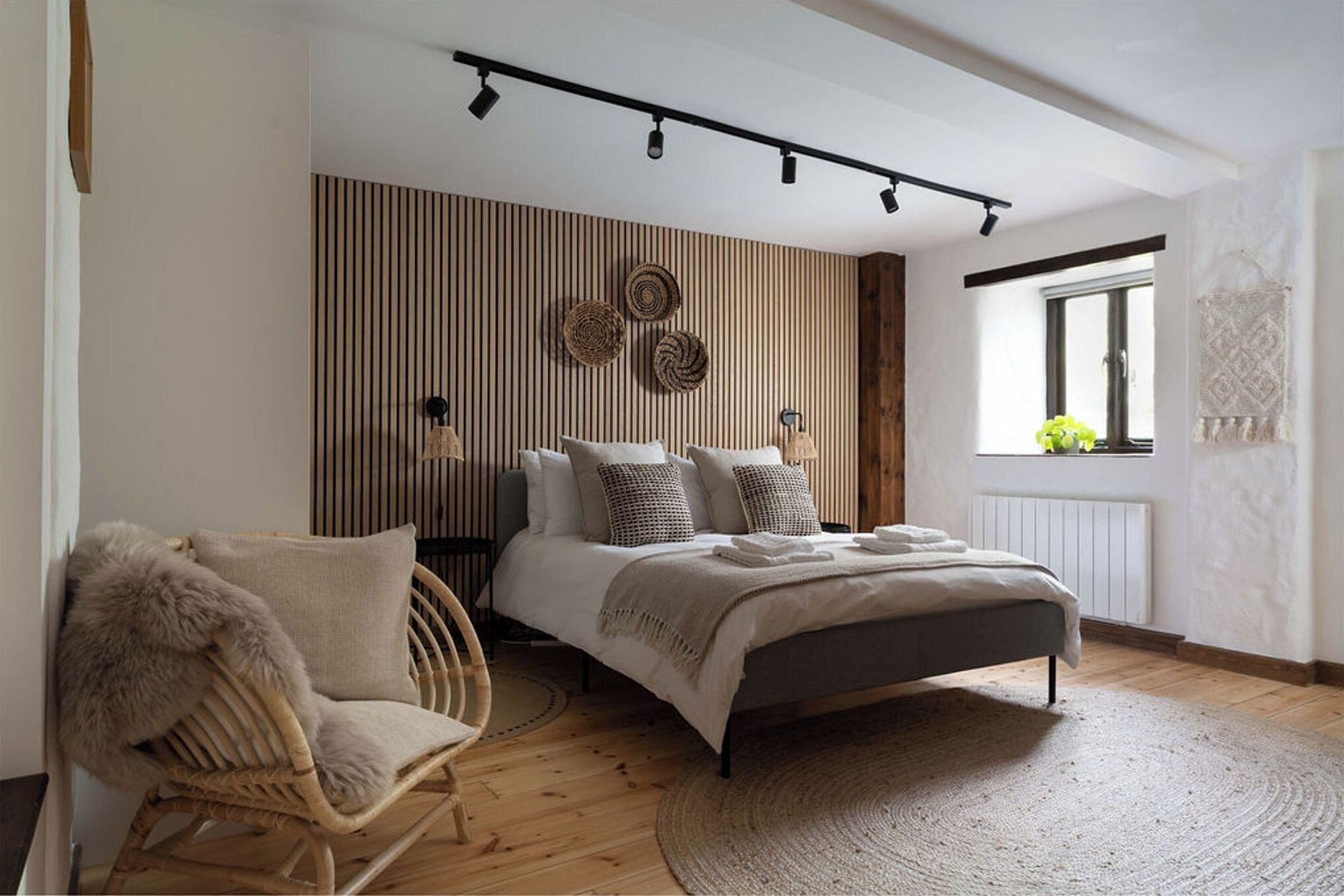 A bedroom with a bed, a chair, a window, and a wall with vertical lines and woven decorations.