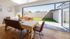 A dining area with a table set for four, a large window with a view of a backyard, and a skylight above. - Delightful Seaside Hideaway 5 Mins to Beach (Chichester)