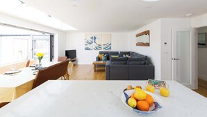 A modern living space with a dining area, a sofa, and a large table with a fruit bowl. - Delightful Seaside Hideaway 5 Mins to Beach (Chichester)