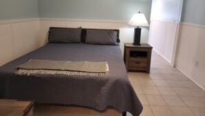 A bedroom with a bed, nightstand, lamp, and a window with a view. - Harrison Hotel Unit F
Pet Friendly 
Ground Level (Murrells Inlet)
