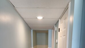 A hallway with white wainscoting, beige tiled flooring, and light blue walls. - Harrison Hotel Unit F
Pet Friendly 
Ground Level (Murrells Inlet)