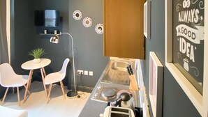 A compact kitchen with a coffee machine, two white chairs, a small table with a plant, and a wall-mounted TV. - Holland Rd Studios Close to Olympia London (London)