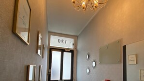A hallway with a chandelier, framed pictures, a door with a sign, and a vase with feathers. - Holland Rd Studios Close to Olympia London (London)