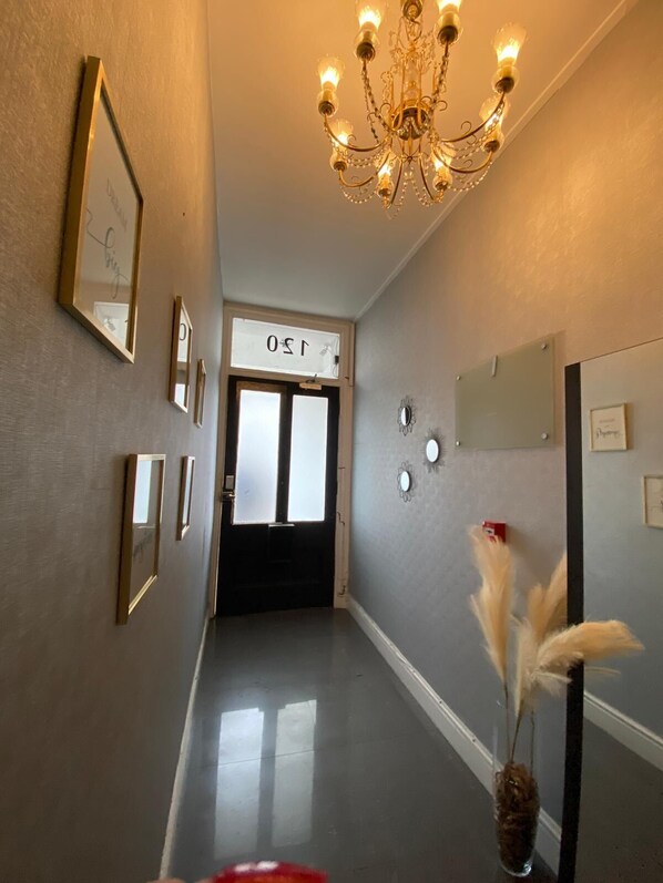 A hallway with a chandelier, framed pictures, a door with a sign, and a vase with feathers. - Holland Rd Studios Close to Olympia London (London)