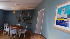 Un comedor con una mesa redonda de madera y sillas blancas, una lámpara en el techo y un cuadro en la pared.