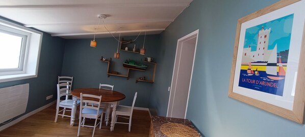 Un comedor con una mesa redonda de madera y sillas blancas, una lámpara en el techo y un cuadro en la pared.