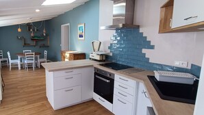 Una cocina moderna con armarios blancos, horno negro y salpicadero de azulejos azules. Se observa una zona de comedor con una mesa y sillas al fondo.