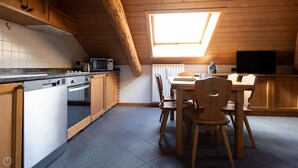 A kitchen with wooden cabinets, a dining table with chairs, a microwave, and a television. - Andreola 1 - Two Bedroom Apartment, Sleeps 6 (Bormio)