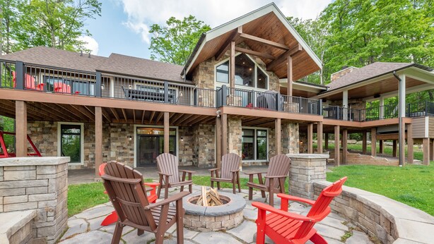 Ein zweistöckiges Haus mit Steinfassade, einer überdachten Terrasse mit Adirondack-Stühlen und einem Feuerkorb.